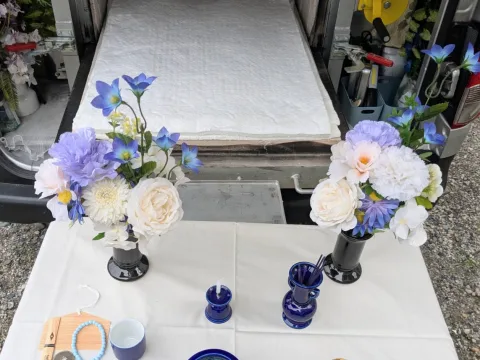 祭壇テーブルの供花と仏具、奥に白い敷布を敷いた火葬炉